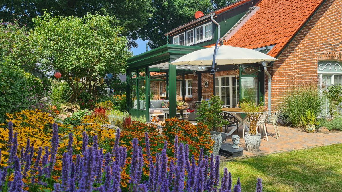 Gebauter Sommergarten mit grünem Rahmen an der Terrasse, davor leuchtende Staudenbeete mit Agastache